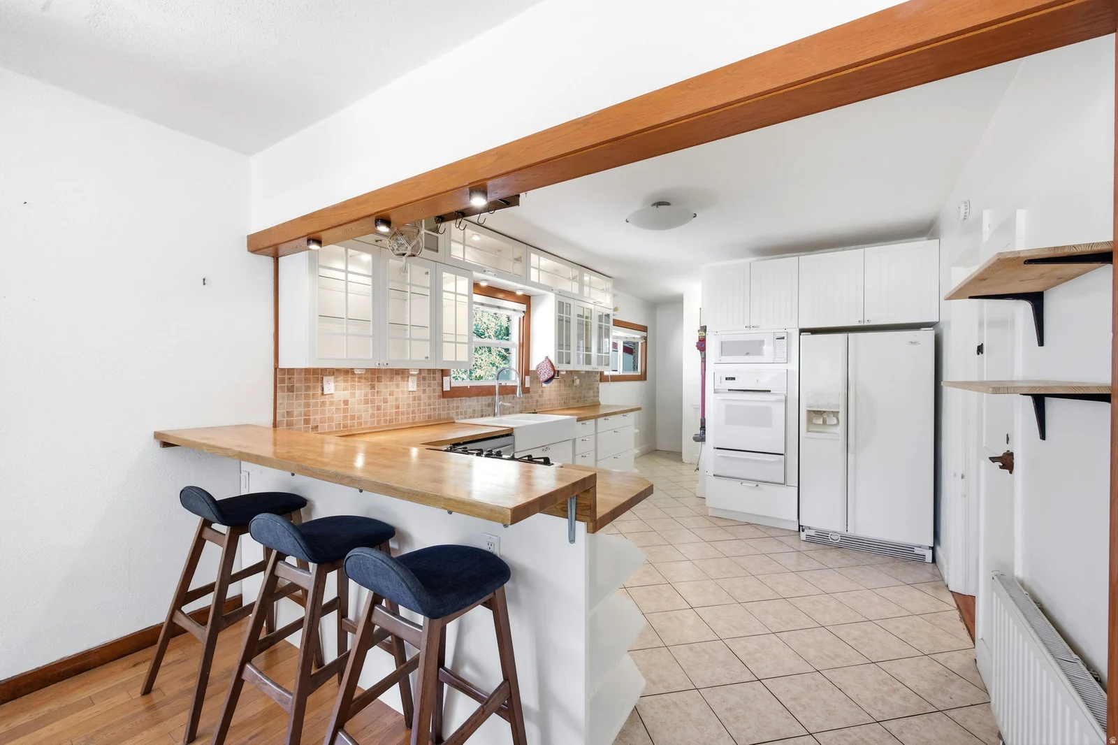 Kitchen featuring a breakfast bar with wood-finish countertop, white cabinetry, integrated built-in appliances, tiled flooring, and a tiled backsplash